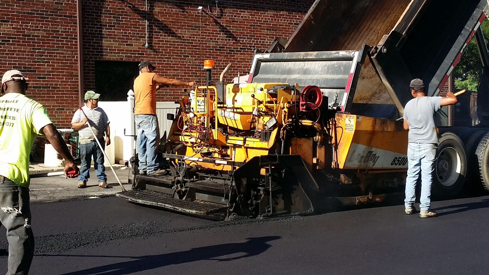 Asphalt paving crew laying blacktop behind a paver and dump truck