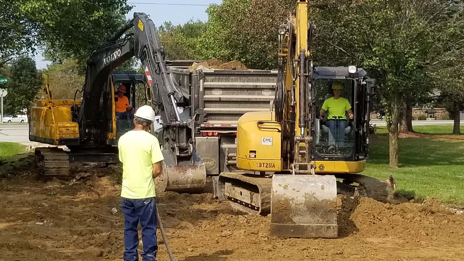 Excavation crew with two excavators and a dump truck digging a utility trench