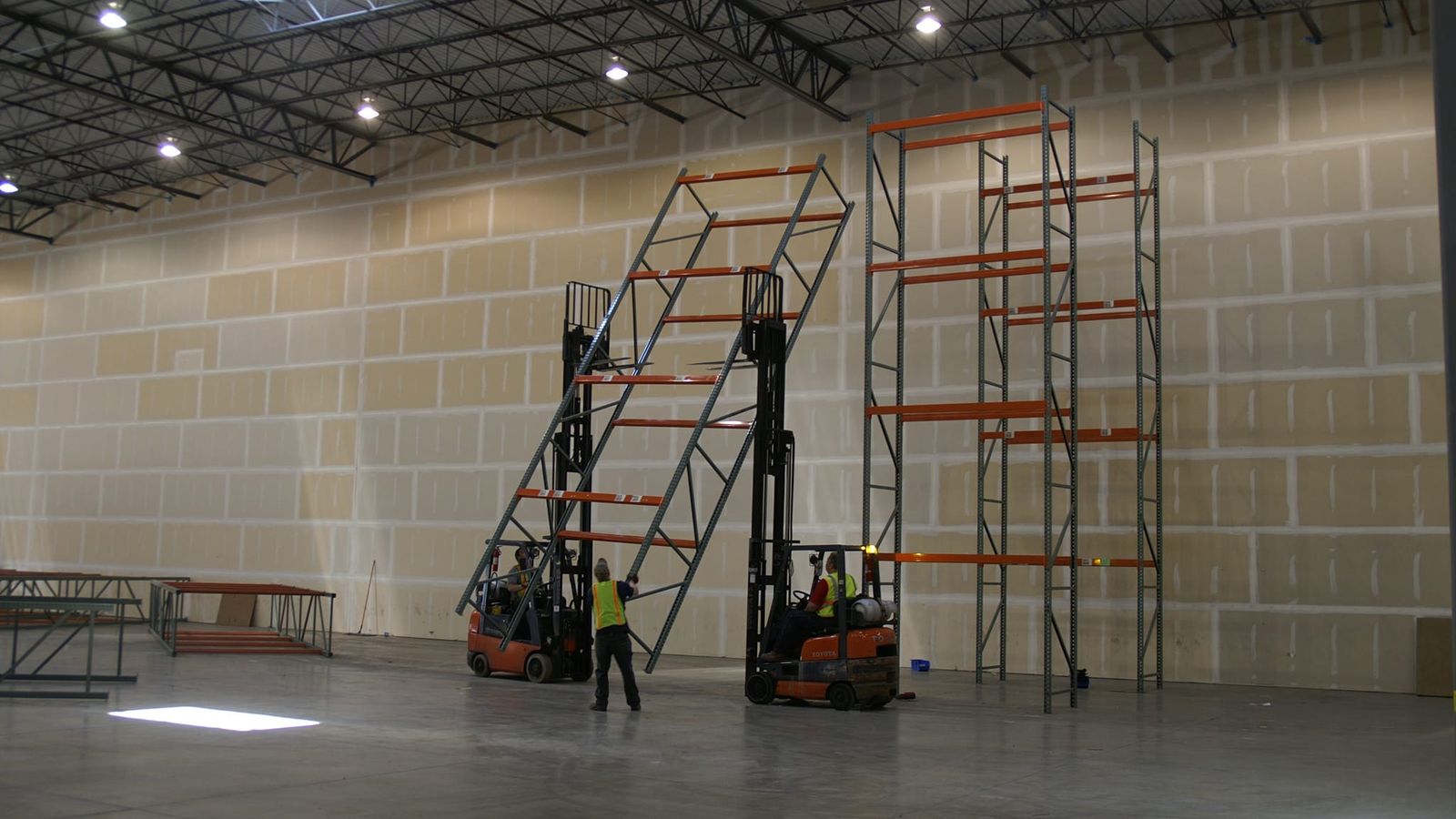 Crew using forklifts to install upright frames for a pallet rack system in a new warehouse