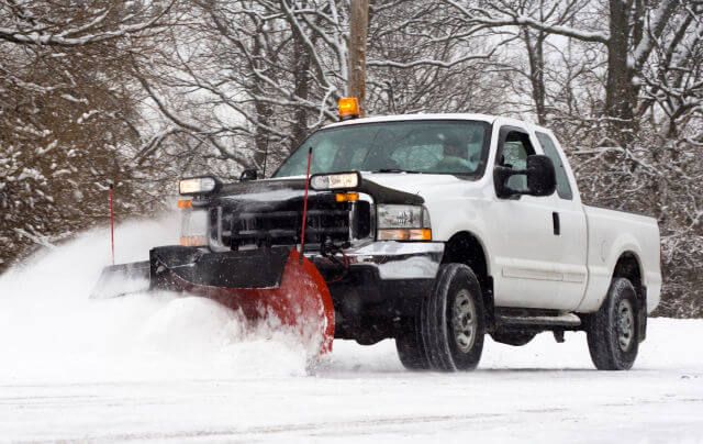 Pickup truck with a snow plow clearing a lot during snowfall